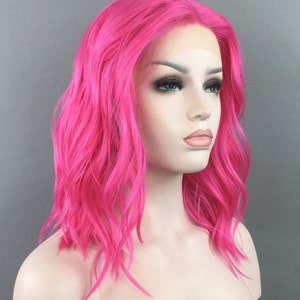 May include: A bright pink, wavy synthetic wig with a lace front. The wig is styled in a shoulder-length bob.