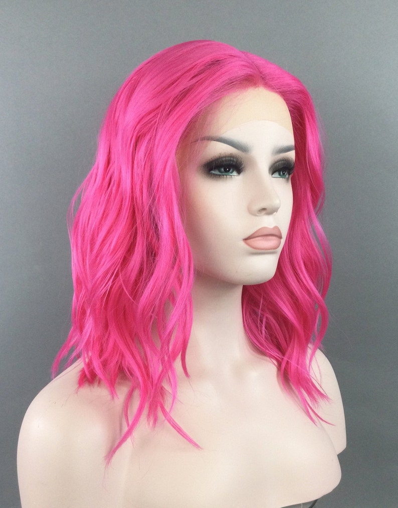 May include: A bright pink, wavy synthetic wig with a lace front. The wig is styled in a shoulder-length bob.