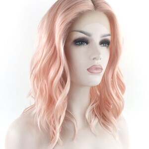 May include: A light pink wig with loose waves. The wig is styled in a medium length bob.