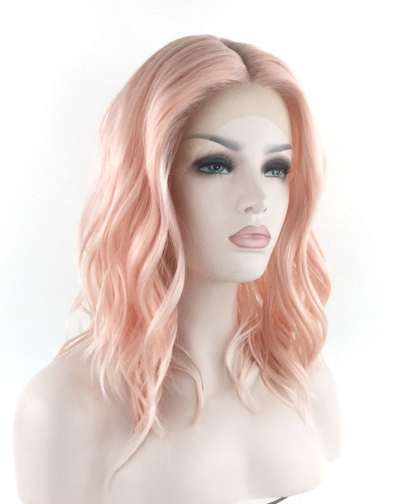 May include: A light pink wig with loose waves. The wig is styled in a medium length bob.