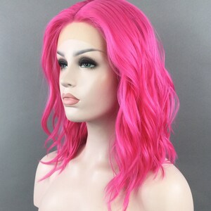 May include: A bright pink, wavy synthetic wig with a lace front. The wig is styled in a shoulder-length bob.