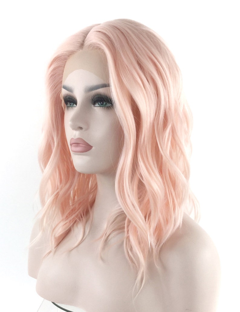 May include: A light pink wavy synthetic wig with a lace front. The wig is styled in a shoulder-length bob with loose waves.