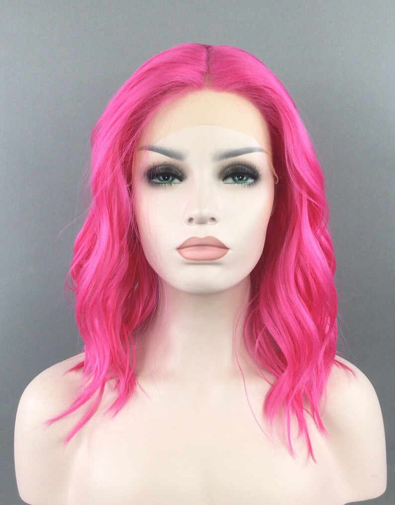 May include: A bright pink, wavy synthetic wig with a lace front. The wig is styled in a shoulder-length bob.
