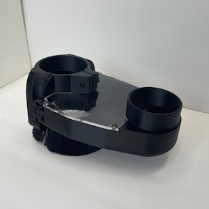 May include: Black dust collection system for a router, featuring a brush and a clear plastic shield.