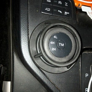 Pode incluir: Close-up de um botão de controle 4WD preto com as opções 4L, 4H, TM e 2H. O botão é cercado por um anel de plástico preto.