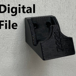 May include: Digital file for a 3D printed wall mount for a controller. The mount is black and has a textured surface.