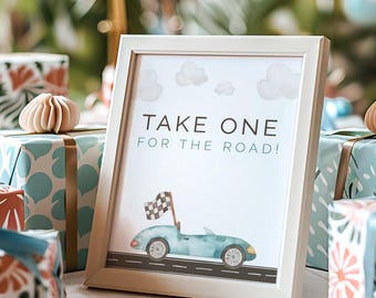 May include: A framed sign with the text "TAKE ONE FOR THE ROAD!" and a watercolor illustration of a blue convertible car. Surrounded by wrapped gifts with ribbons and decorative paper.