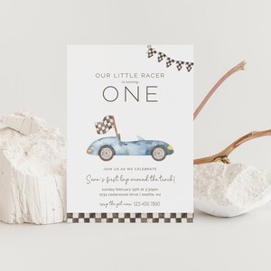May include: A blue and white race car birthday invitation with a checkered flag banner and the text "Our Little Racer is turning ONE. Join us as we celebrate Sean's first lap around the track!"
