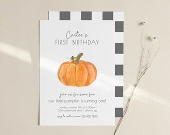 May include: A white invitation card with a black and white checkered pattern on the right side. The card features a watercolor illustration of an orange pumpkin with a small green frog on top. The text on the card reads "Carter's First Birthday" and includes details about the birthday party, including the date, time, and location. The text also includes the phrase "Join us for some fun our little pumpkin is turning one!"