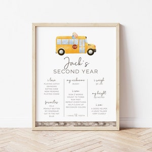 Könnte beinhalten: Ein gerahmter Druck mit einer Illustration eines gelben Schulbusses. Der Druck enthält den Text "Jack's SECOND YEAR" und persönliche Details wie Gewicht (13,6 kg), Größe (73,7 cm) und Lieblingsdinge. Der untere Rand hat ein Straßendesign.
