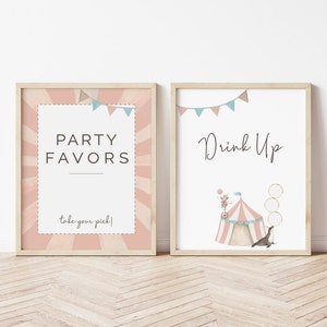May include: Two printable signs with a circus theme. The sign on the left says "Party Favors" with a pink and white striped background. The sign on the right says "Drink Up" with a circus tent and a seal balancing balls.