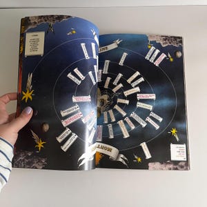 May include: An open book with a black background and a spiral design. The spiral is made up of white rectangles with text on them. The text is in a white font. The book is open to a page that says "MONOLITH".