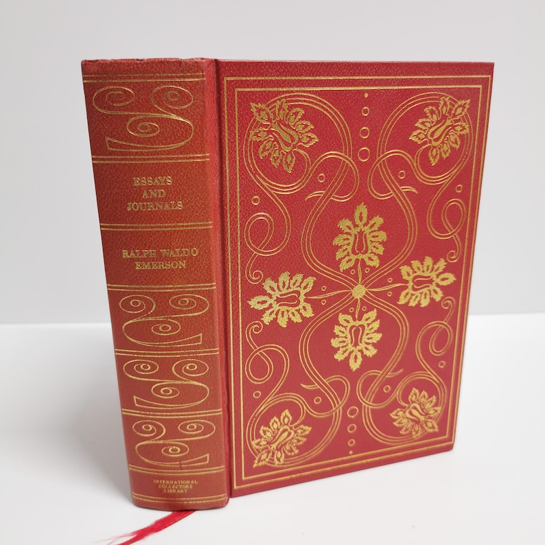 May include: A red hardcover book with gold lettering on the spine. The title is "Essays and Journals" by Ralph Waldo Emerson. The cover features a gold floral design.
