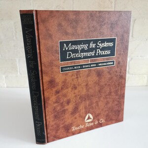 May include: A brown leather-bound book titled "Managing the Systems Development Process" by Charles L. Biggs, Evan G. Birks, and William Atkins. The book is published by Touche Ross & Co.