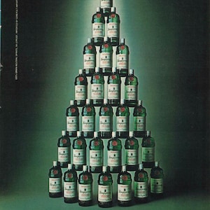 Op de afbeelding: Een kerstboom gevormd door groene Tanqueray Gin-flessen met witte etiketten en rode zegels. De afbeelding bevat de tekst: "Suddenly, the idea of importing a Christmas tree from England begins to make sense."