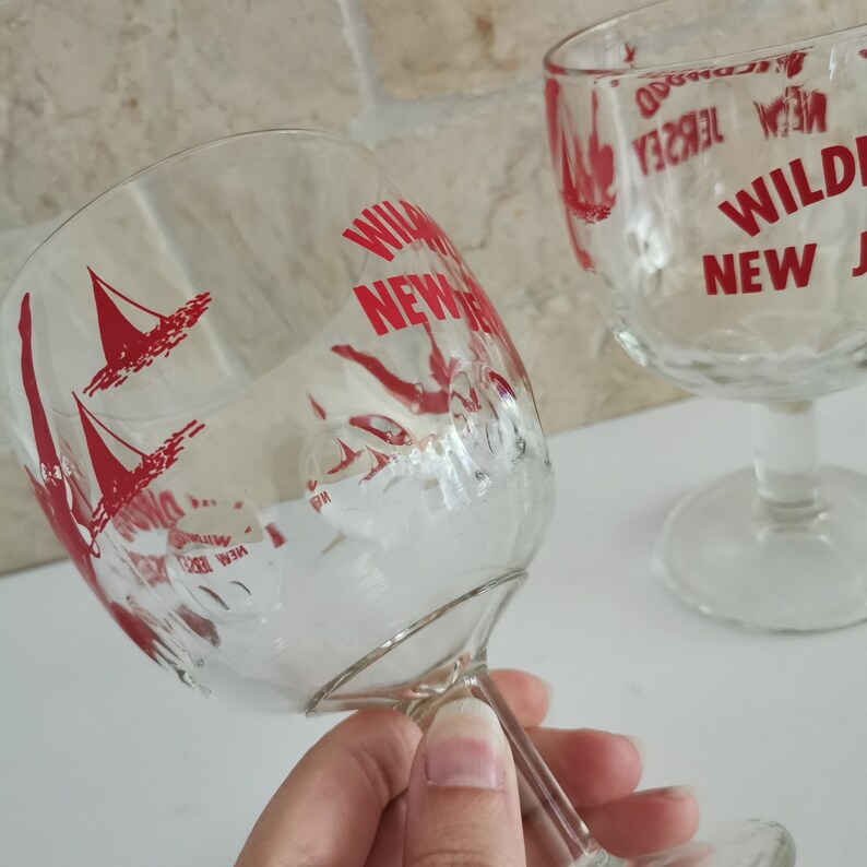 May include: Two clear glass goblets with red lettering that says "Wildwood New Jersey". One goblet has a sailboat design.
