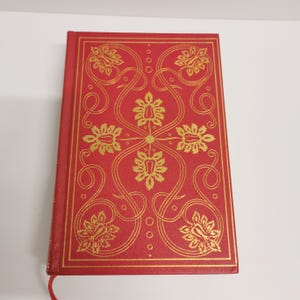 May include: A red hardcover book with a gold floral design on the cover.
