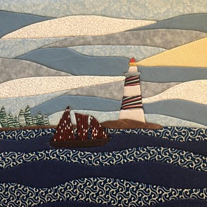 May include: A fabric wall hanging featuring a quilted landscape scene with a lighthouse, a sailboat with dark red sails, and a forest of green trees. The sky is composed of layered blue and white patterned fabric, while the ocean is dark blue.