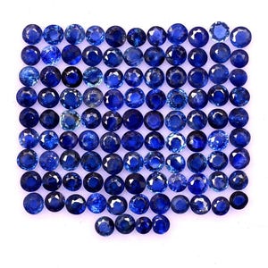 May include: A collection of numerous round, faceted blue sapphire gemstones arranged in a grid pattern. Each stone displays a brilliant cut with multiple facets that reflect light, showcasing various shades of deep, vibrant, and royal blue hues.