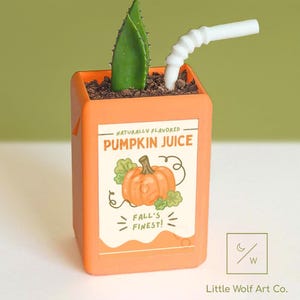 May include: Orange planter shaped like a juice box, with the text "Limited Time Only!" above. The planter features a green plant and a white straw. The label reads "Pumpkin Juice" with a pumpkin illustration. The bottom right corner has a logo and the text "Little Wolf Art Co."