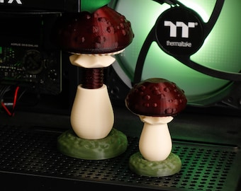 May include: Two 3D-printed mushroom sculptures featuring dark red caps with raised spots, cream-colored stems, and textured green bases. The taller mushroom has a visible threaded stem design, while the shorter one has a smooth, solid stem structure.