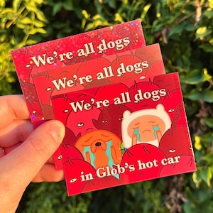 May include: Three red stickers with the text "We're all dogs" and a cartoon image of a dog in a car. The bottom sticker has the text "in Glob's hot car".