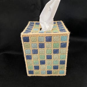May include: A square tissue box cover with a woven pattern in shades of blue, green, and beige. The top opening dispenses a white tissue. The box is a decorative item for the home.