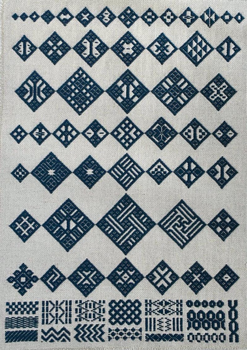 May include: A piece of light beige fabric featuring a collection of dark blue cross-stitch embroidery patterns. The design consists of multiple rows of geometric diamond shapes, each containing unique, intricate, and symmetrical line motifs.