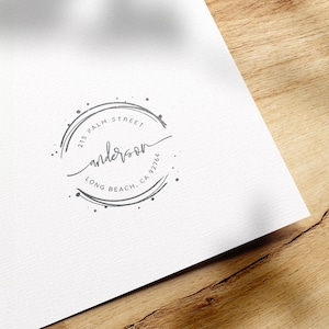 May include: A black and white logo with the text "anderson" in cursive script. The logo is surrounded by a circle with the text "215 PALM STREET LONG BEACH, CA 927164".