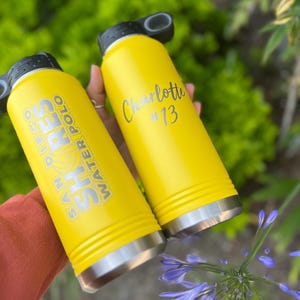 May include: Two yellow water bottles with black lids and silver bottoms. One bottle has "SAN DIEGO SHORES WATER POLO" printed on it. The other bottle has the name "Charlotte" and the number "13" printed on it.