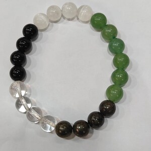 May include: A beaded bracelet featuring a variety of colorful gemstones. The bracelet includes black, white, clear, green, and brown beads. The beads are round and appear to be polished. The bracelet is displayed on a white surface.