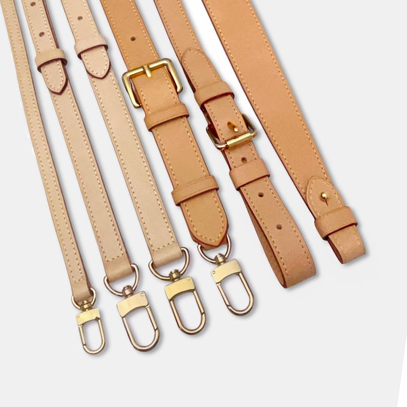 May include: Assortment of leather bag straps in various shades of beige and tan. The straps feature gold-colored metal hardware, including buckles and clasps. The straps are of different lengths and widths, with visible stitching.