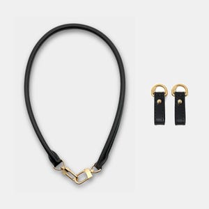 May include: Black leather handbag strap with gold-tone hardware, including a clasp and D-rings. Two matching black leather D-ring connectors with gold-tone hardware are also shown.