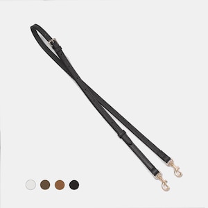 May include: Black leather bag strap with gold-coloured metal clasps and buckles. The strap is thin and appears to be adjustable. The image shows the strap against a neutral background.
