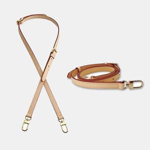 May include: Two beige leather purse straps with gold-colored hardware. One strap is crossed, and the other is coiled. Both straps have adjustable buckles and swivel clasps for easy attachment to a bag.