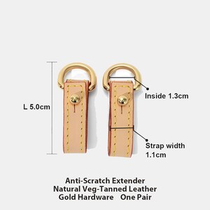 May include: Two natural veg-tanned leather strap extenders with gold hardware. Each extender is 5.0cm long, with a strap width of 1.1cm and an inside diameter of 1.3cm. The text reads: Anti-Scratch Extender, Natural Veg-Tanned Leather, Gold Hardware, One Pair.