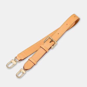 May include: A tan leather bag strap with gold-coloured metal hardware. The strap has a buckle for adjustment and two swivel clasps for attachment. The leather appears smooth and the stitching is visible along the edges.