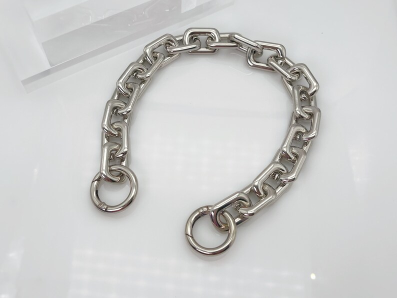 May include: A silver chain necklace with a large, chunky link design. The chain has two circular clasps.