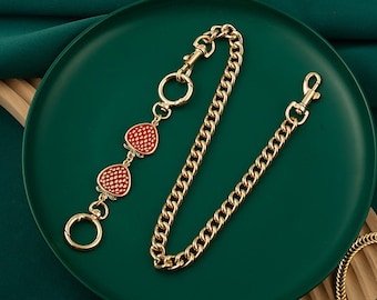 May include: A gold chain with a lobster clasp and three red strawberry charms. The chain is on a green background.