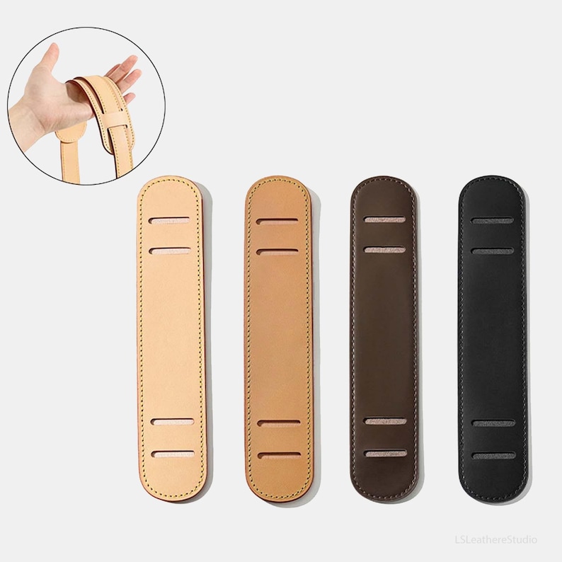 May include: Four leather shoulder pads in varying shades of brown and black. Each pad has two parallel slots for strap attachment and is rectangular with rounded ends. The pads are designed to provide comfort and support for bags or straps.