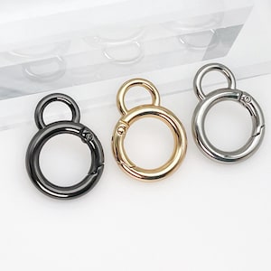 May include: Three metal keyrings with a swivel clasp and a double ring design. The keyrings are in gold, silver, and black.