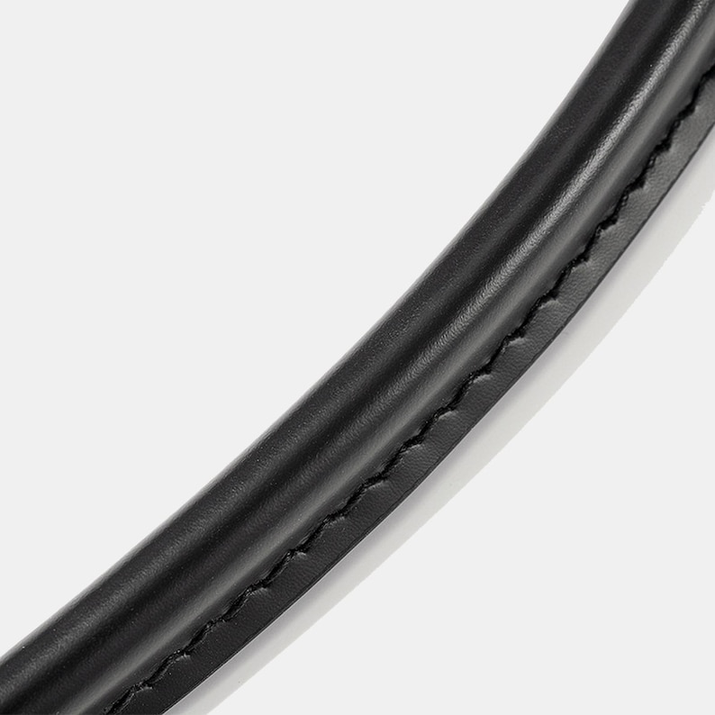 May include: Close-up of a curved, black leather handle with visible stitching. The handle appears smooth and slightly glossy, suggesting a high-quality material. The stitching is a contrasting color, adding detail to the design.