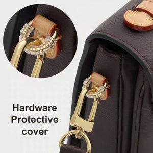 May include: Close-up of a gold-toned hardware protective cover for a handbag. The cover is designed to protect the hardware from scratches and wear. The cover is made of a clear, flexible material and is easy to apply and remove.