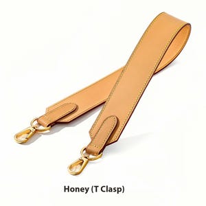 May include: A honey-colored leather bag strap with gold-tone clasps. The strap features a T-clasp design and is stitched with a contrasting thread. The text "Honey (T Clasp)" is displayed at the bottom of the image.
