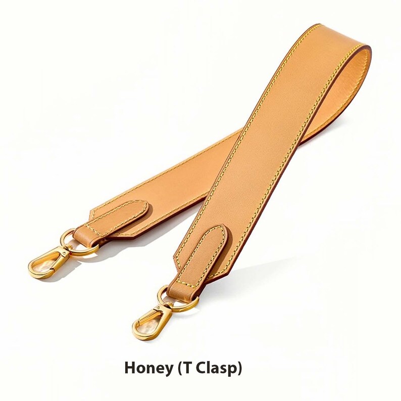 May include: A honey-colored leather bag strap with gold-tone clasps. The strap features a T-clasp design and is stitched with a contrasting thread. The text "Honey (T Clasp)" is displayed at the bottom of the image.