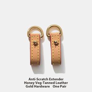 May include: Two honey-colored leather Anti-Scratch Extenders with gold hardware and stitching. Each extender has a gold-colored metal ring at the top and a gold button. The text on the image reads: Anti-Scratch Extender, Honey Veg-Tanned Leather, Gold Hardware, One Pair.