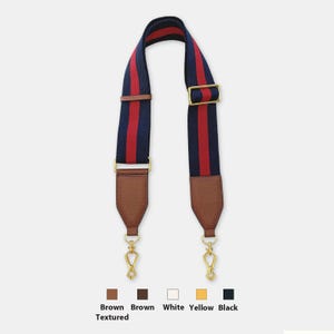 May include: A navy blue and red striped bag strap with brown leather accents. The strap has gold-colored metal hardware, including clasps and a buckle. The bottom of the strap has brown textured leather.