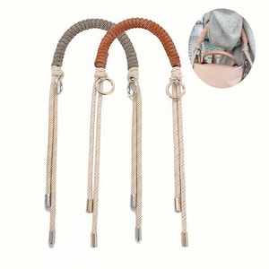 May include: Two purse handles with a rope design. One handle is brown and the other is gray. The handles have cream-colored rope straps with metal accents and gold-colored rings. The handles are shown against a white background.