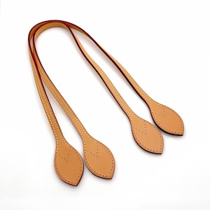 May include: Tan leather purse handles with red edges and decorative stitching. The handles have a leaf-shaped design at the ends with multiple small holes for attachment. The handles are set against a white background.