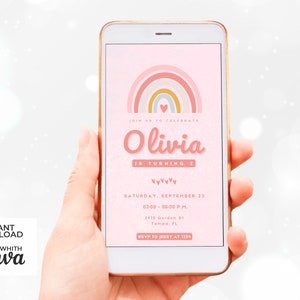Op de afbeelding: Een roze en gele regenboog-verjaardagsuitnodiging met de tekst "Vier met ons mee Olivia wordt 2 jaar" en details voor het feest. De uitnodiging wordt weergegeven op een smartphone-scherm.